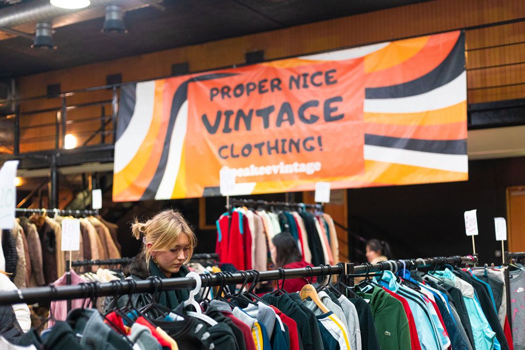 A photograph of a vintage clothes market with a student browsing through items on a rail