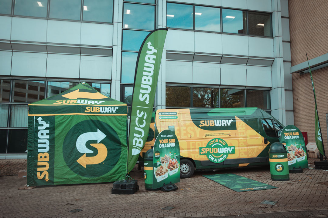 A Subway tent and van parked outside the union building with branded flags